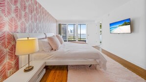 A modern bedroom with a bed, a nightstand, a lamp, a TV, and a city view.