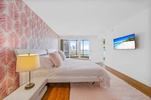 A modern bedroom with a bed, a nightstand, a lamp, a TV, and a city view.