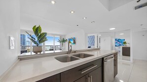 A modern kitchen with a double sink, dark cabinetry, and a large window offering a city view.