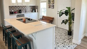 A modern kitchen with a central island, bar stools, a bench, and a large potted plant.