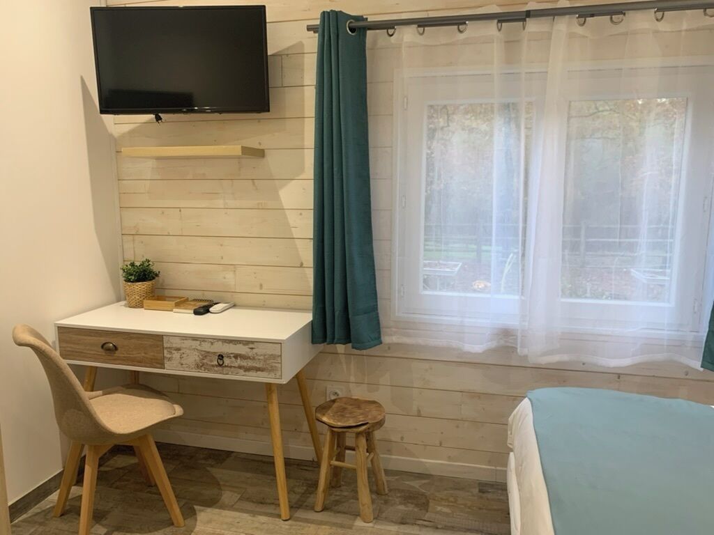 Una habitación con escritorio, silla, televisión y ventana con cortinas.