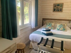 Una stanza con un letto, una finestra con tende, un muro in legno e un piccolo sgabello.