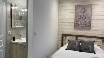 A bedroom with a bed, a nightstand, a mirror, a sink, and a wall-mounted artwork.
