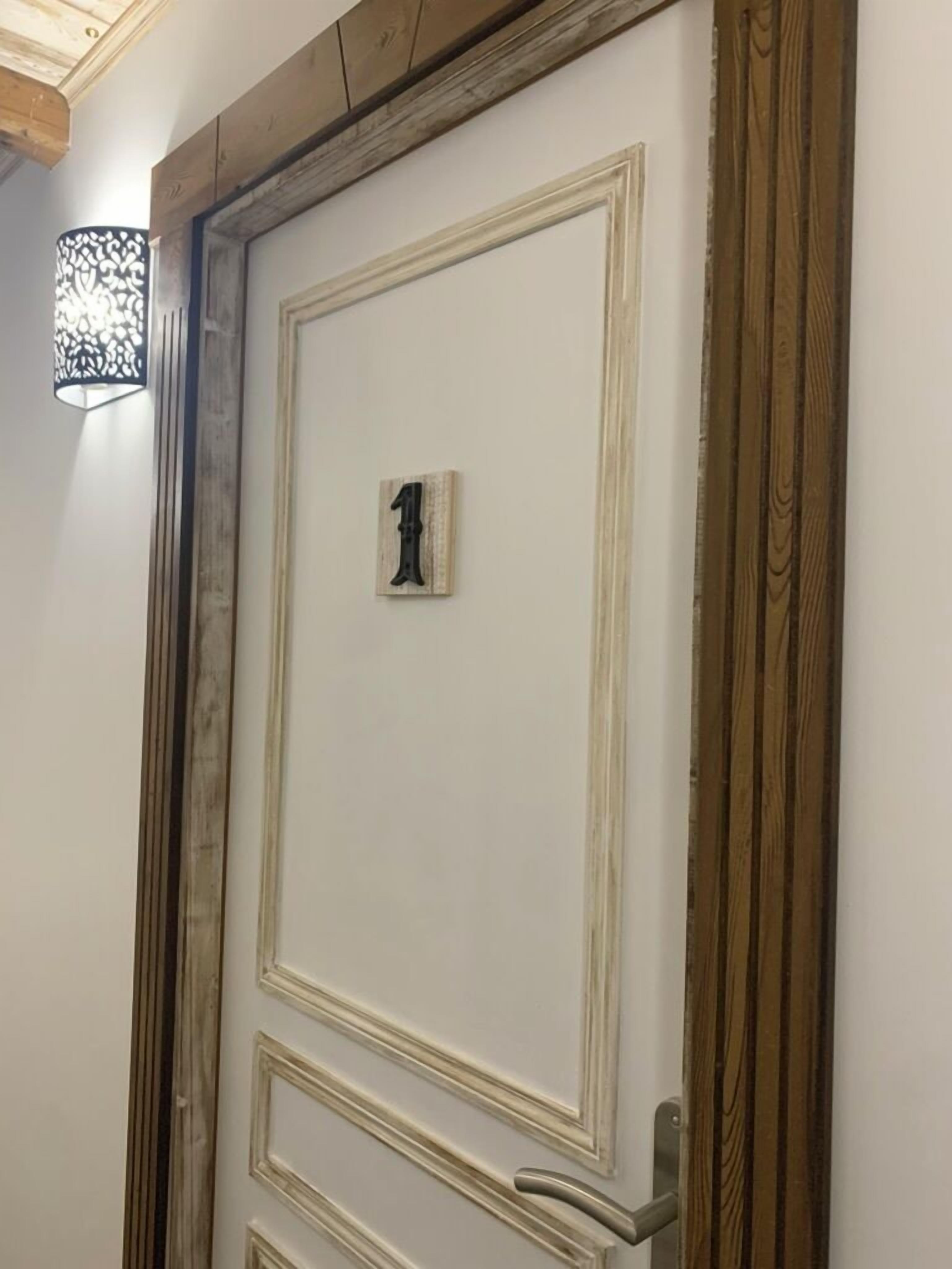 A door with a number plate, a wooden frame, and a wall-mounted light fixture.