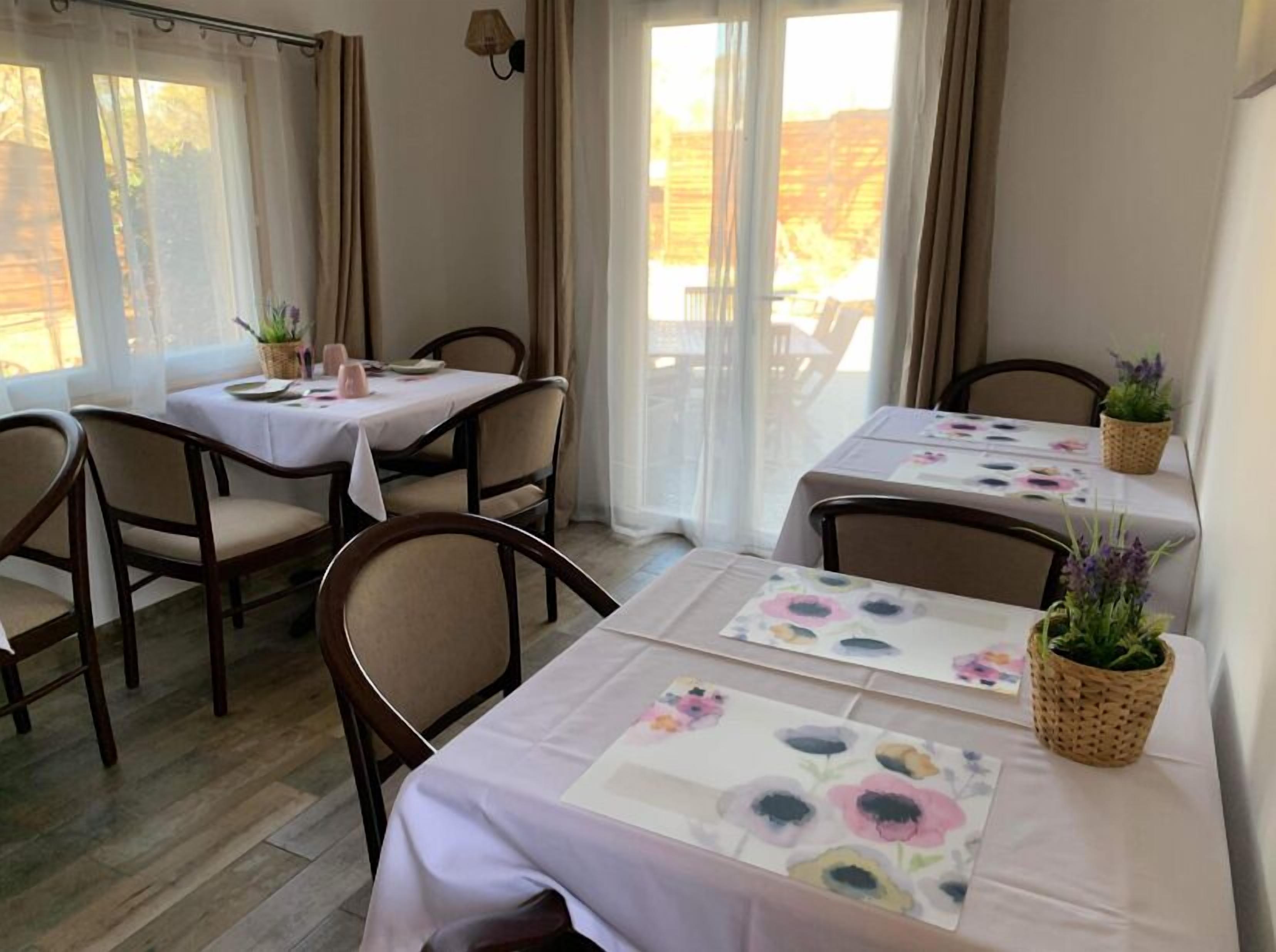 A dining area with tables set for two, chairs, and potted plants.