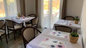 A dining area with tables set for two, chairs, and potted plants.