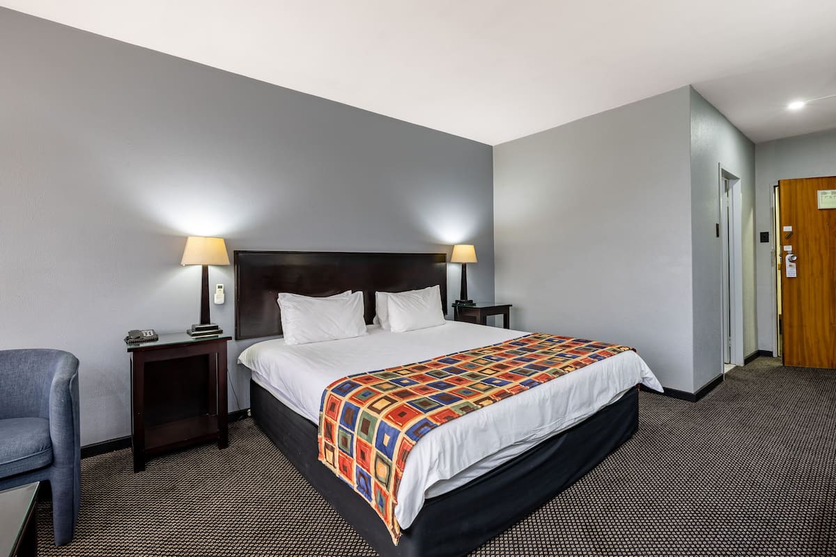 A hotel room with a large bed, two bedside tables, a chair, and a door.