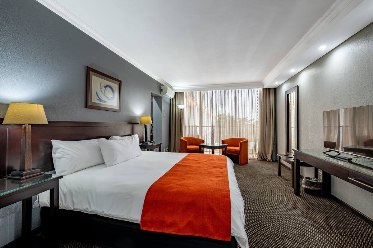 A hotel room with a large bed, two chairs, a desk, and a TV.