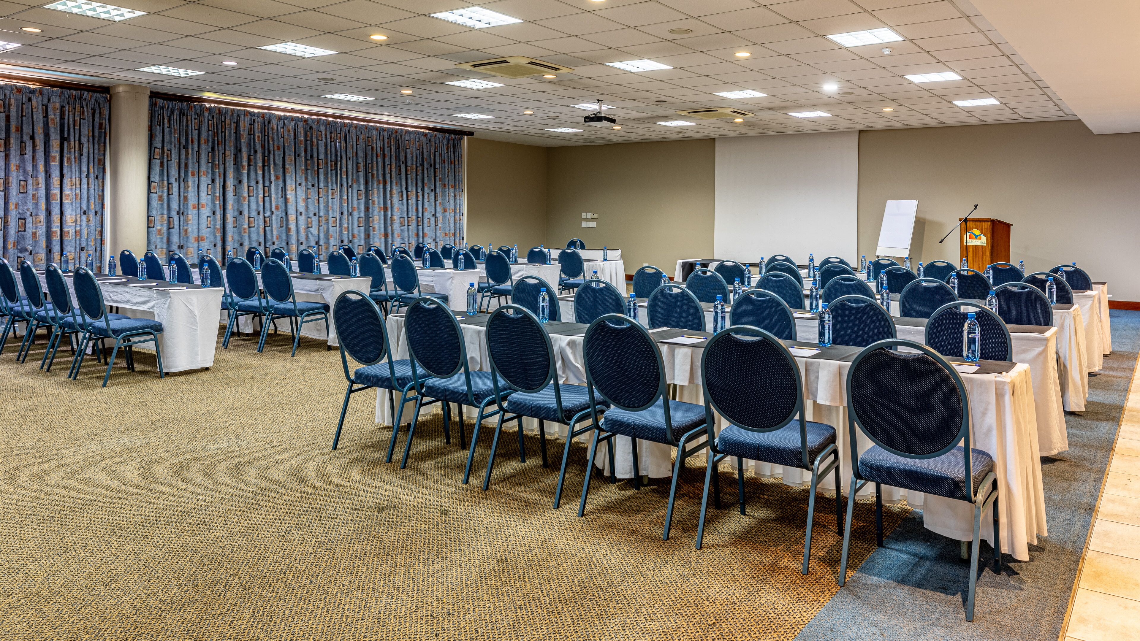 A conference room with rows of tables and chairs, a projector, and a podium.