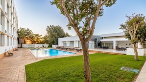A swimming pool with lounge chairs, a grassy area, and a building with multiple windows and a covered patio. - African Sky Hotels - Ermelo Inn (Ermelo)