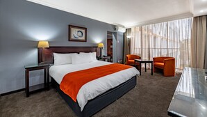 A hotel room with a large bed, two chairs, a small table, and a glass partition. - African Sky Hotels - Ermelo Inn (Ermelo)