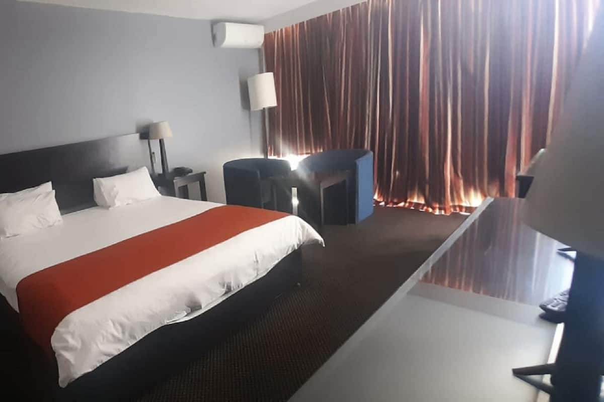A hotel room with a large bed, two bedside tables with lamps, a desk with a chair, and a view of a curtain.