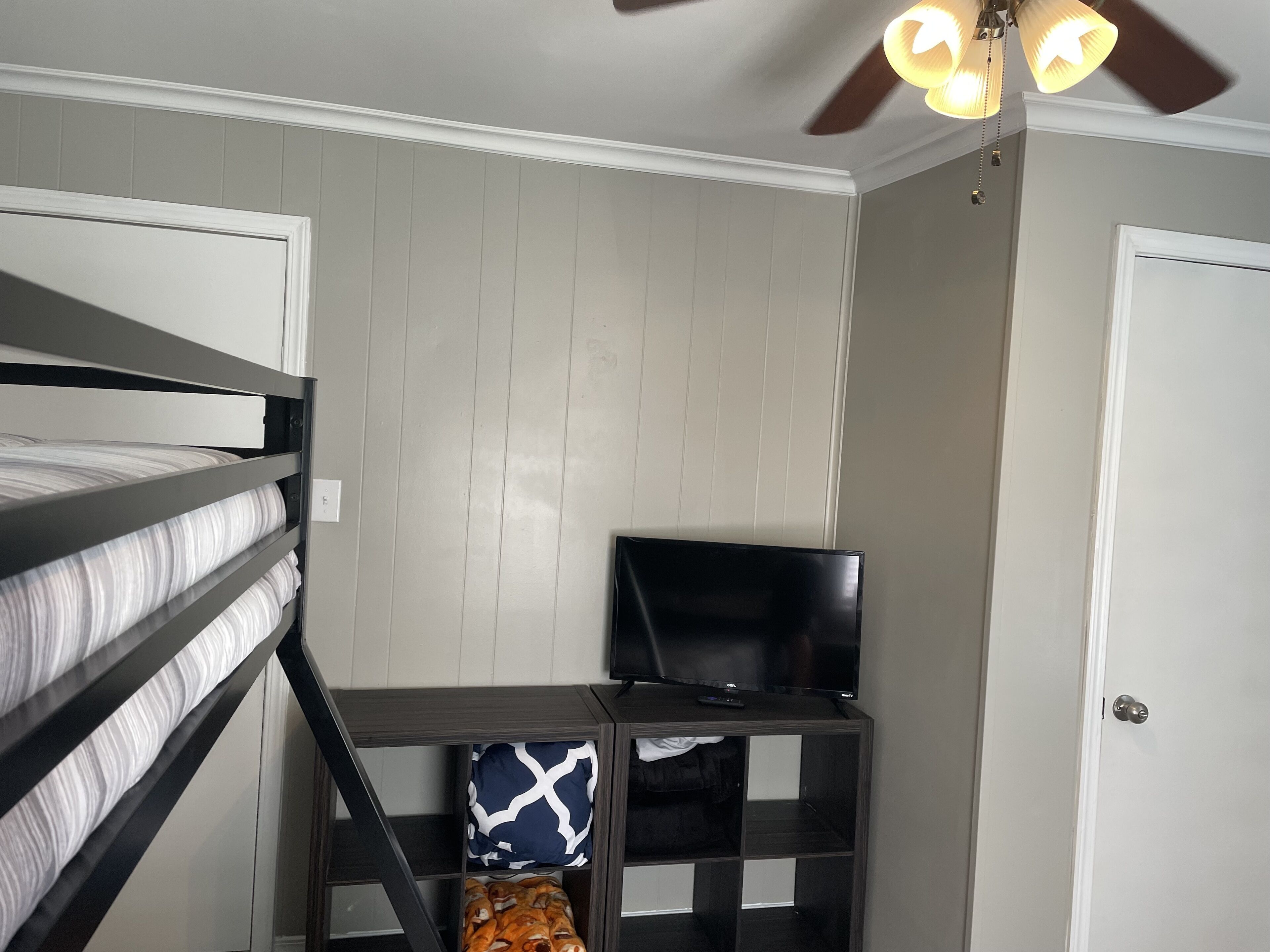A bedroom with a bunk bed, a TV on a shelf, and a ceiling fan.