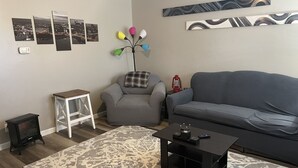 A living room with a grey sofa, a small white table, a patterned rug, and a black coffee table.