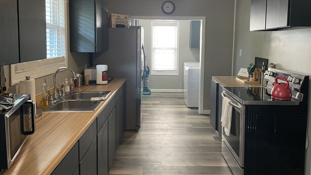 A modern kitchen with a wooden countertop, stainless steel appliances, and a ceiling fan.