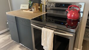 A compact kitchen with a stainless steel range and oven, a wooden countertop, and a red kettle.