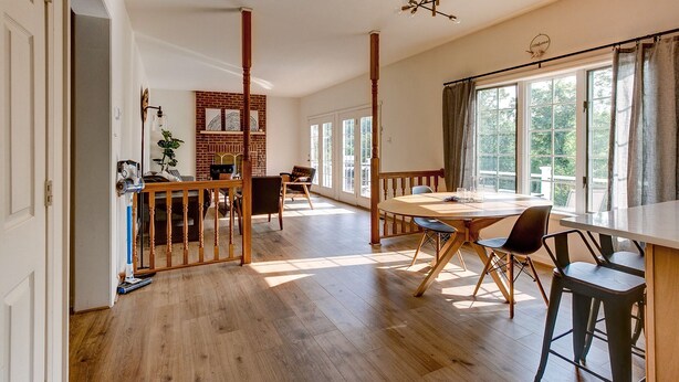 A spacious room with a large dining table, wooden chairs, and a view of the outdoors through large windows.