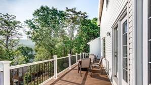 A wooden deck with a white railing, a table, and chairs, overlooking a forested area.