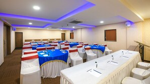 A conference room with rows of tables, white chairs, and blue tablecloths. - King's Kraft Stay Inn Rajkot (Rajkot)
