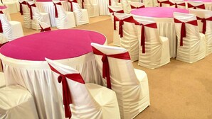 Round tables with white tablecloths and red sashes, arranged in rows. - King's Kraft Stay Inn Rajkot (Rajkot)