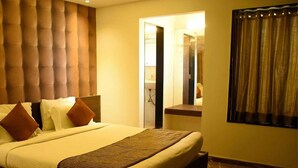 A hotel room with a large bed, a headboard, a bedside table, a mirror, and a window with curtains. - King's Kraft Stay Inn Rajkot (Rajkot)