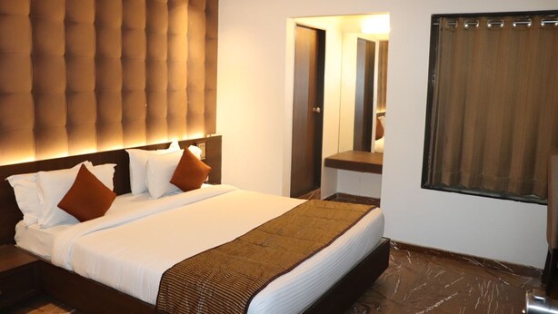 A hotel room with a large bed, a tufted headboard, a mirror, and a window with curtains. - King's Kraft Stay Inn Rajkot (Rajkot)