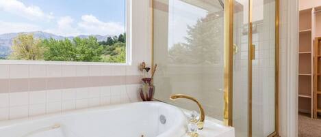 Un baño con una bañera grande, ducha con mampara de vidrio y vistas a zonas verdes y montañas.