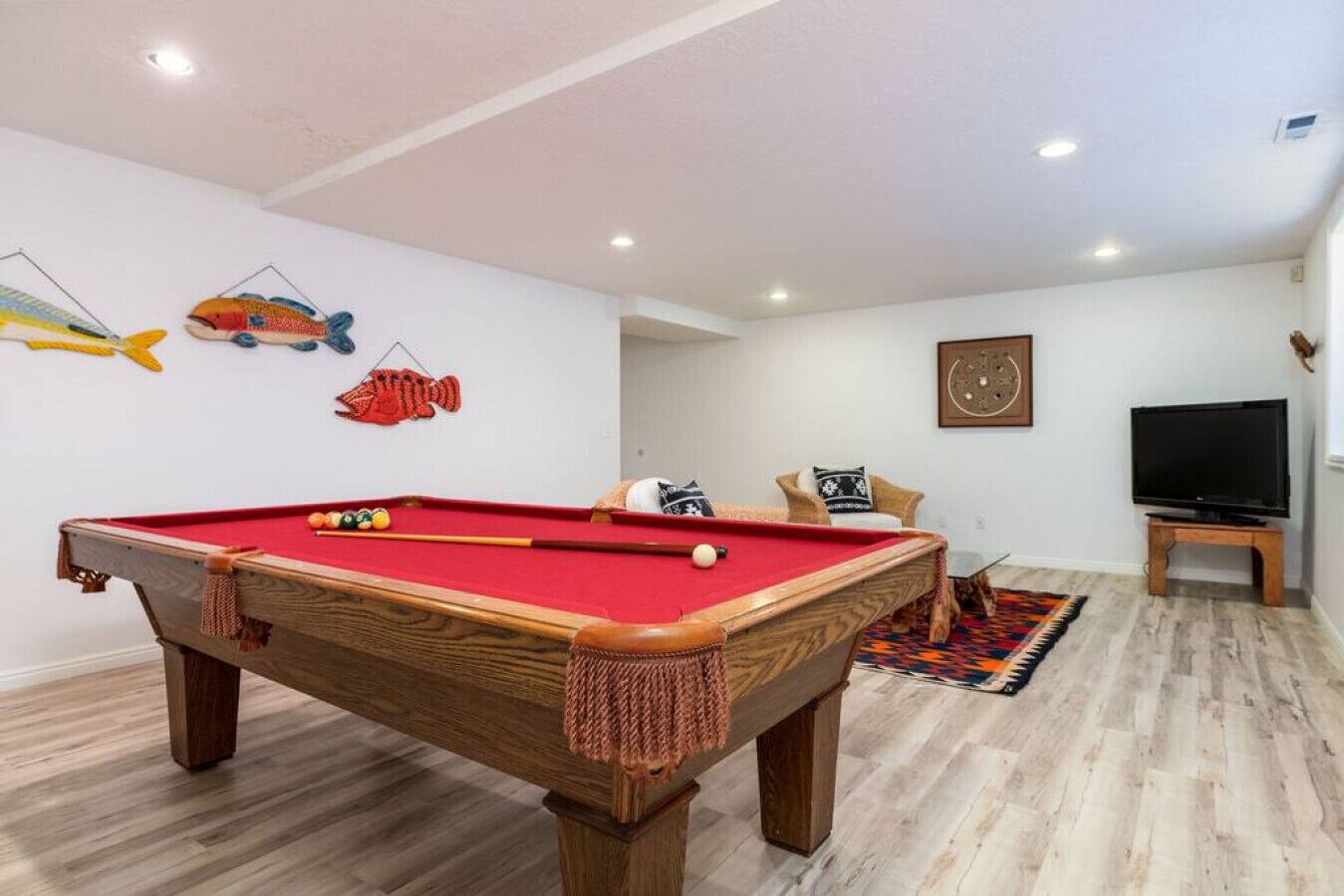 A pool table in a room with wooden flooring, a television, and a patterned rug.