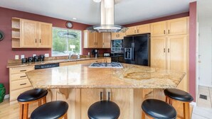 A modern kitchen with a large island, wooden cabinets, stainless steel appliances, and a bar stool seating area. - Wasatch Oaks Retreat (Cottonwood Heights)