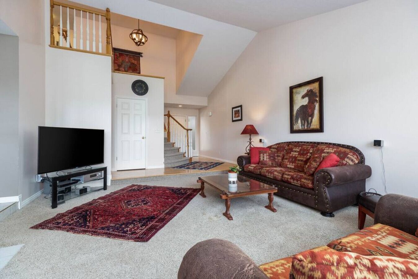 Un salon avec un téléviseur, un canapé et une table basse. Un escalier mène à un autre étage.