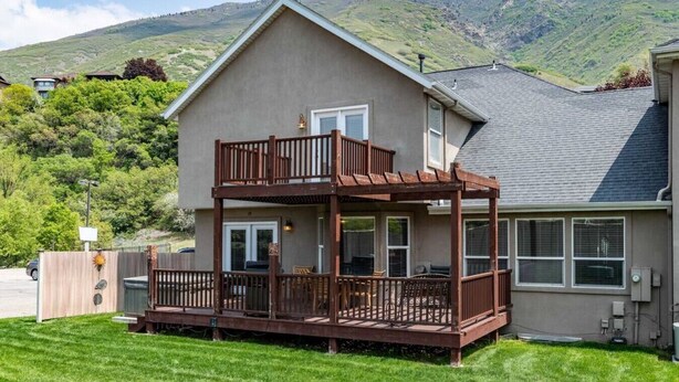 A two-story house with a deck, surrounded by a well-maintained lawn and mountains in the background. - Wasatch Oaks Retreat (Cottonwood Heights)
