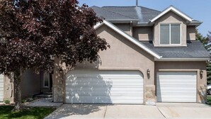 A two-story house with a garage, a tree in front, and a clear sky. - Wasatch Oaks Retreat (Cottonwood Heights)