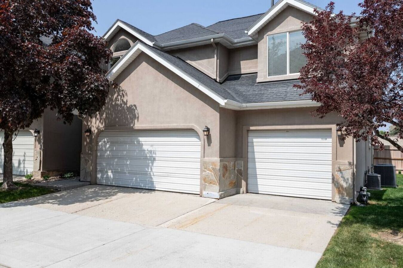 A two-story house with a garage, a stone accent wall, and a well-maintained lawn.
