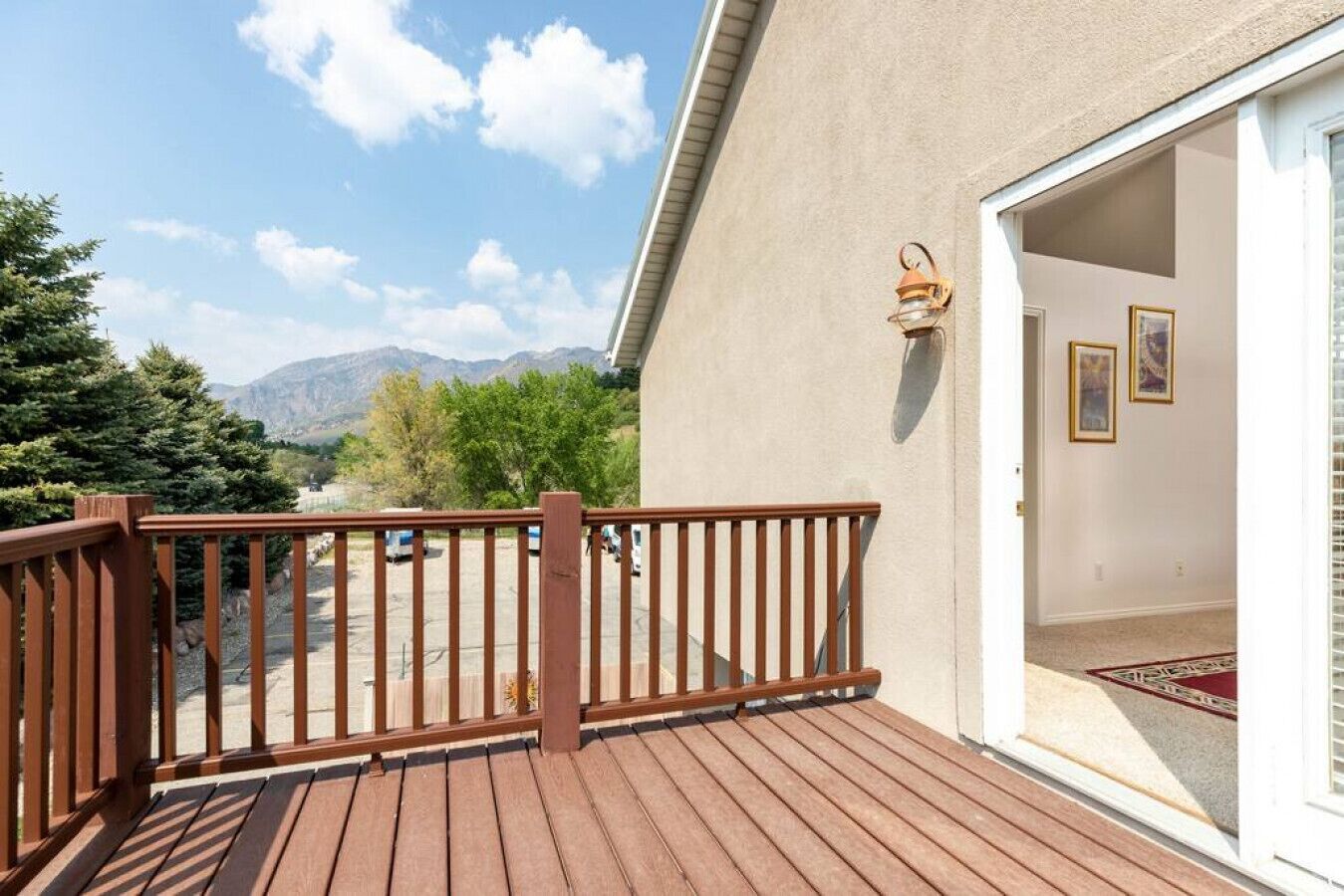 Una terraza de madera con vistas a montañas, una puerta con una lámpara y cuadros en la pared.