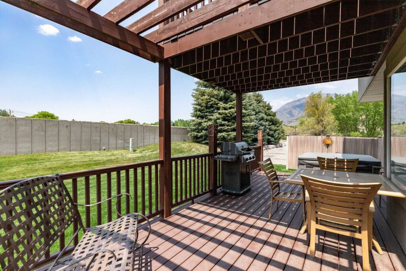 A covered patio with a grill, outdoor seating, and a view of a backyard.