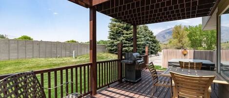 A covered patio with a grill, outdoor seating, and a view of a backyard.