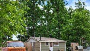 A small house with a garage, a parked orange van, and a tree in the foreground. - Rustic and Eclectic open floor Plan Cabin with Canal view In Cranberry lake 😋.  (Harrison)