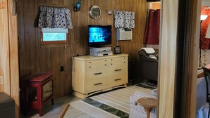 A wooden-paneled room with a television, a small cabinet, and a red stool. - Rustic and Eclectic open floor Plan Cabin with Canal view In Cranberry lake 😋.  (Harrison)