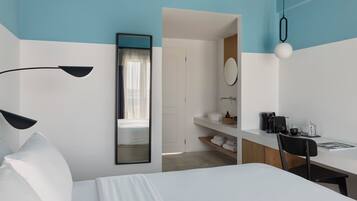 Une chambre d’hôtel équipée d’un lit, d’un bureau, d’une chaise, d’un miroir, d’un lavabo et d’une machine à café.