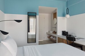 A hotel room with a bed, a desk, a chair, a mirror, a sink, and a coffee maker. - Play Paros, a member of Brown Hotels (Paros)