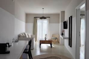 A modern living room with a sofa, a coffee table, and a dining area with a table and chairs. - Play Paros, a member of Brown Hotels (Paros)