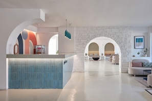 A modern lobby with a reception desk, seating area, and a stone wall. - Play Paros, a member of Brown Hotels (Paros)
