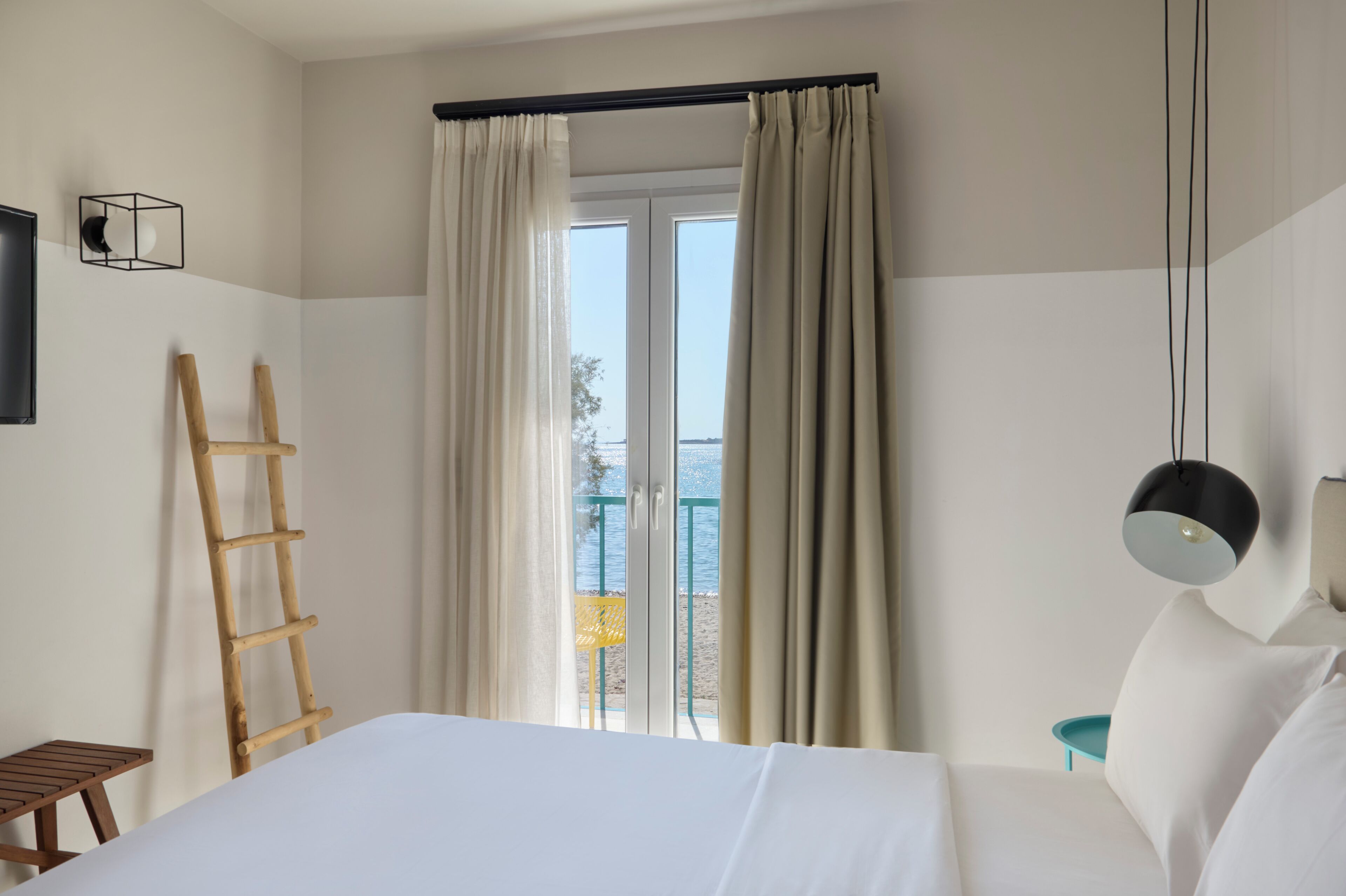 A hotel room with a bed, a wooden ladder, a window with curtains, and a view of the outdoors.
