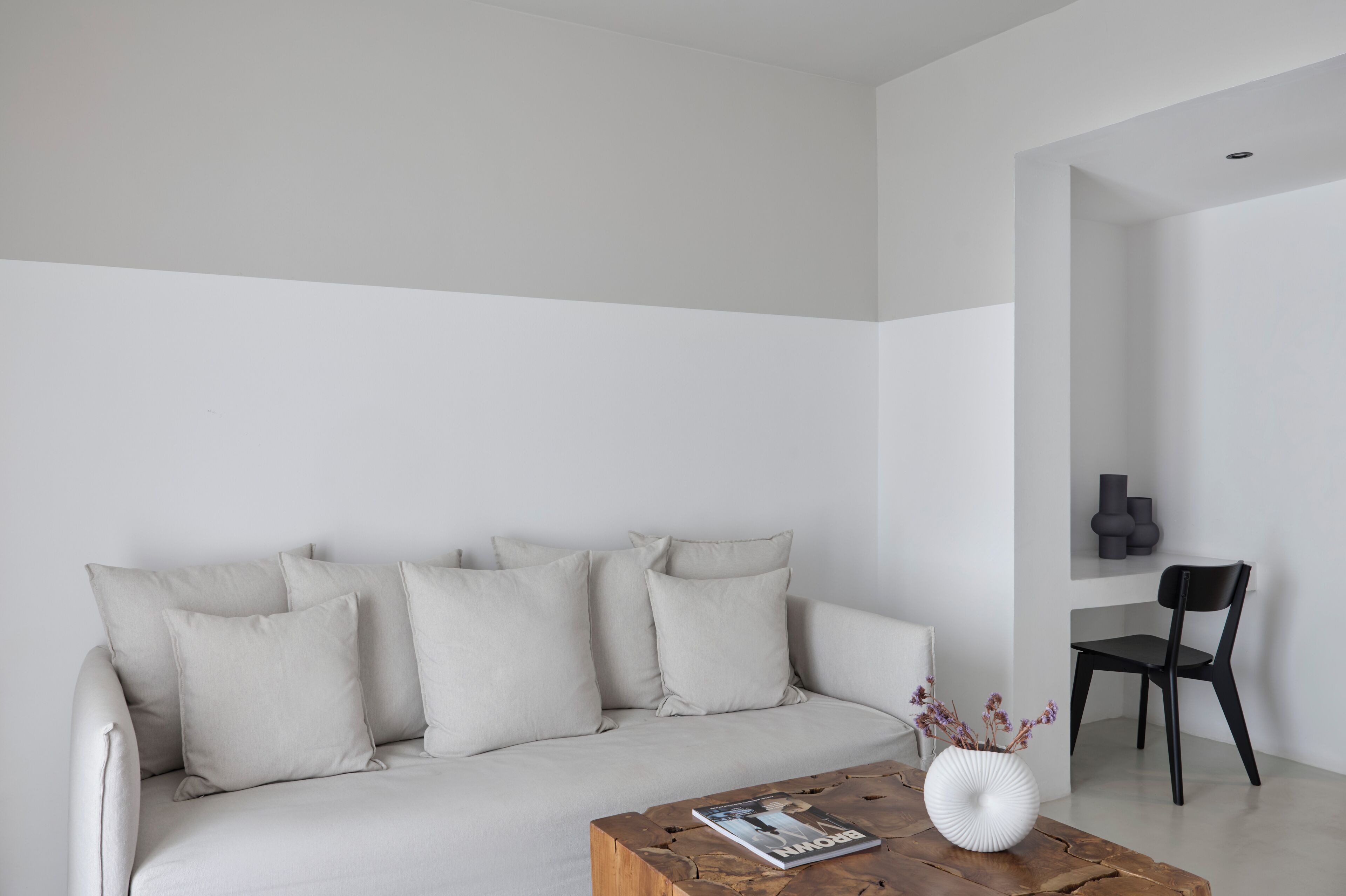 A minimalist living room with a sofa, a coffee table with a magazine, and a vase with flowers.