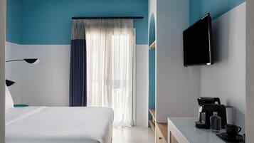 A hotel room with a bed, a desk with a coffee maker, a TV, and a window with curtains.