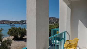 A balcony with a view of boats on the water, a beach, and a hillside in the background.