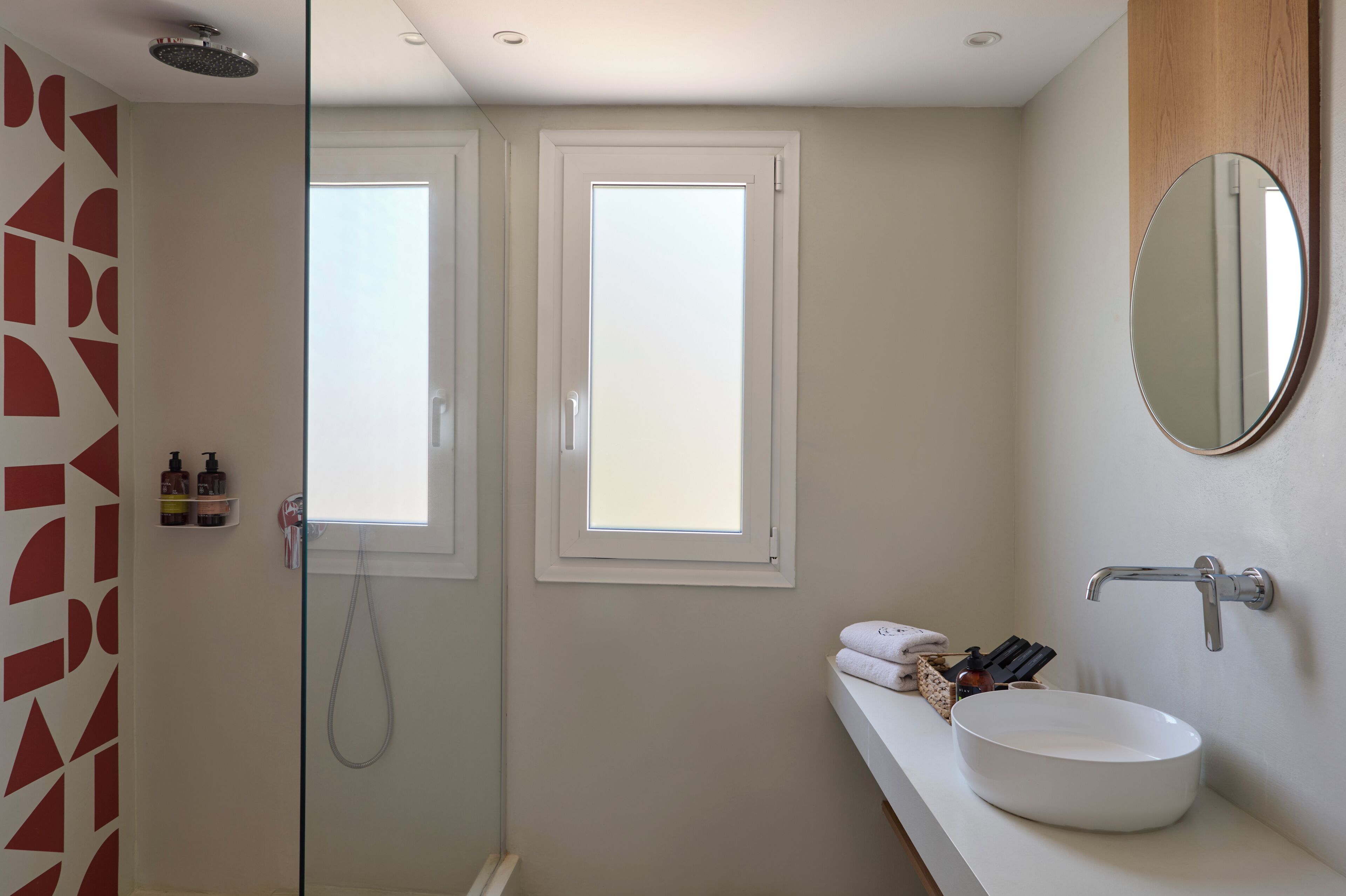 Een moderne badkamer met een douchecabine van glas, een wit wastafelmeubel met spiegel en twee ramen voor natuurlijk licht.