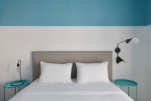 Una cama con cabecera, dos almohadas blancas, una lámpara de noche y dos mesitas redondas.