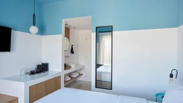 Un dormitorio moderno con cama, mesita de noche y un baño visible a través de una puerta abierta.