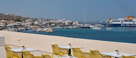 A coastal view with a Blue Star Ferries ship docked, yellow outdoor seating, and a marina with boats.
